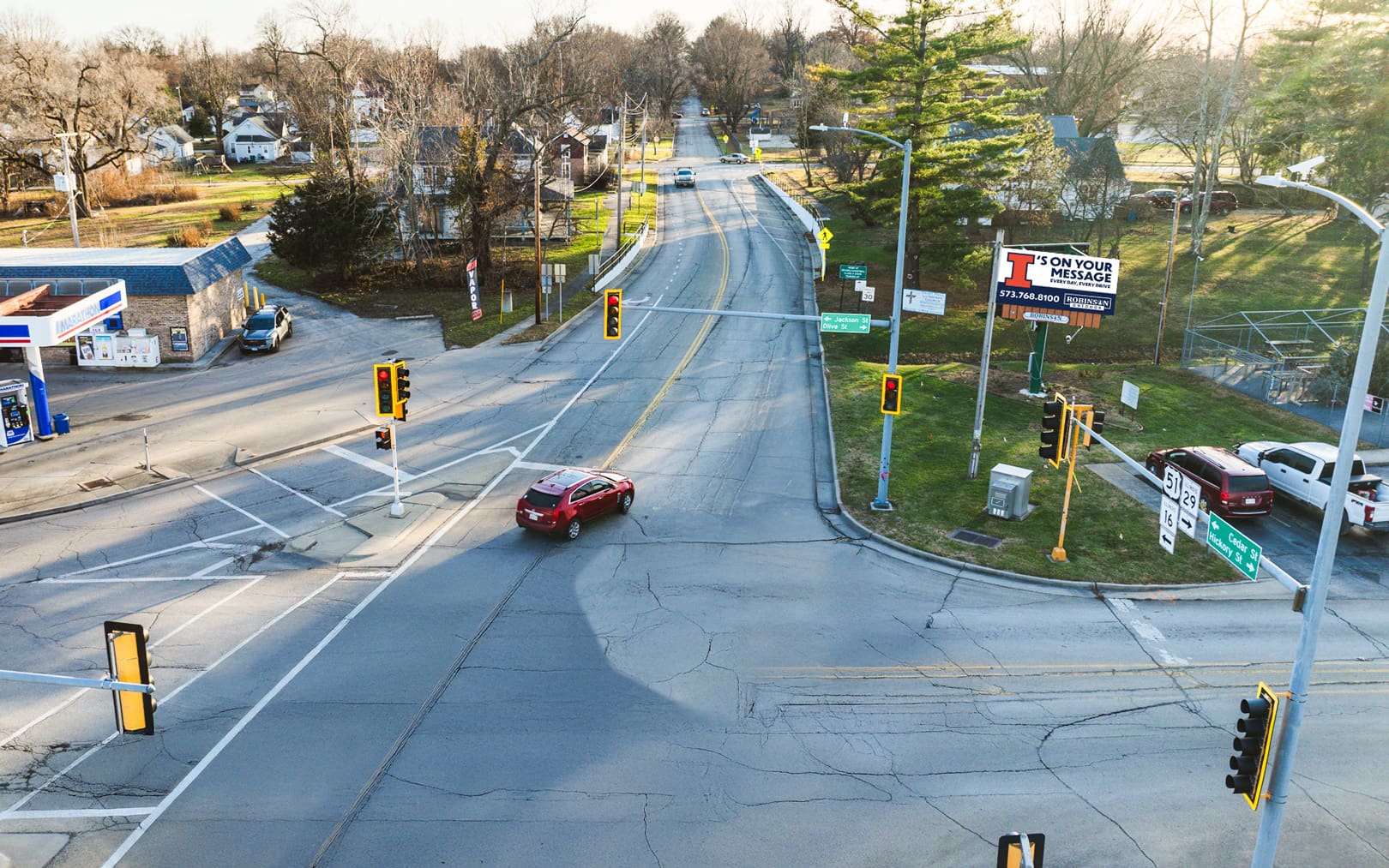 A red car driving down the middle of an intersection.